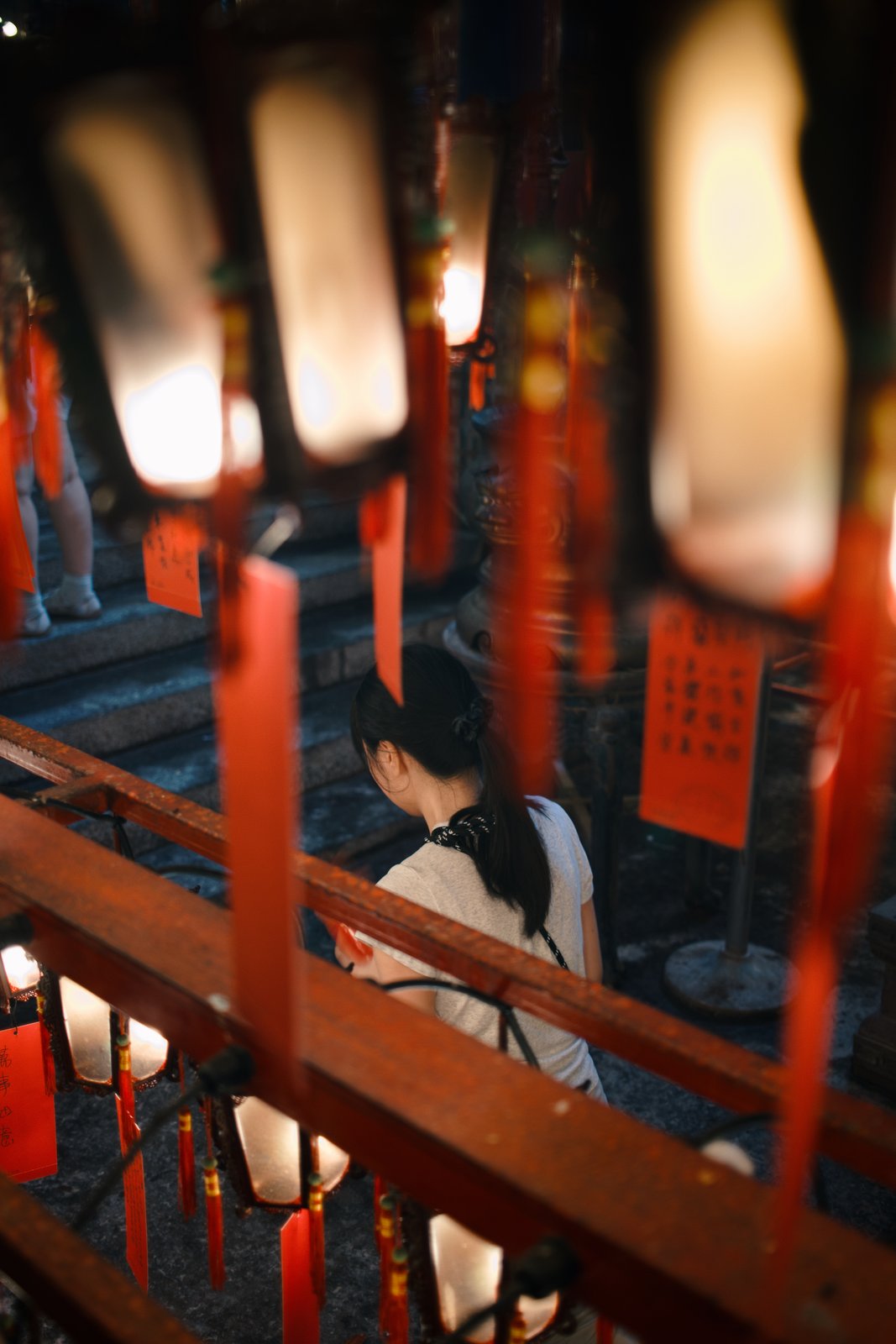 A woman climbing temple stairs behind glowing lanterns and red tassels