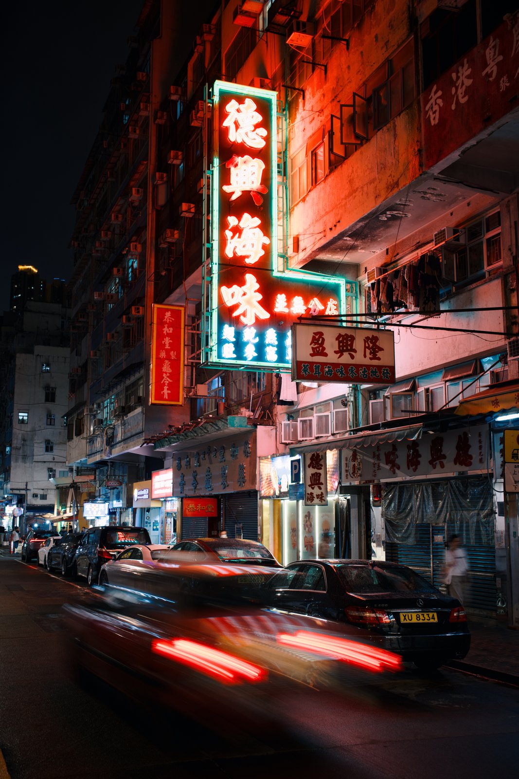 A neon sign glowing above a street as a car streaks past