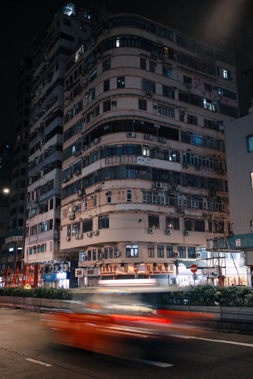 A curved residential block at night with a red taxi blurred in front