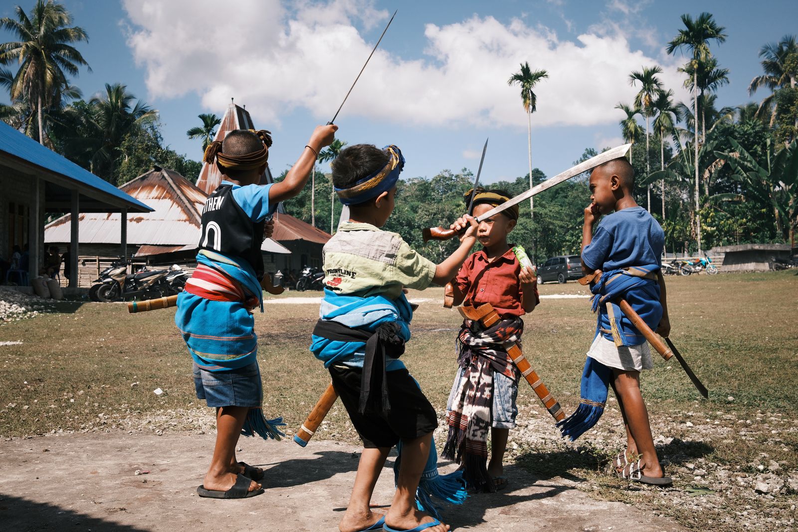 Children mid-dance with blades under palm trees