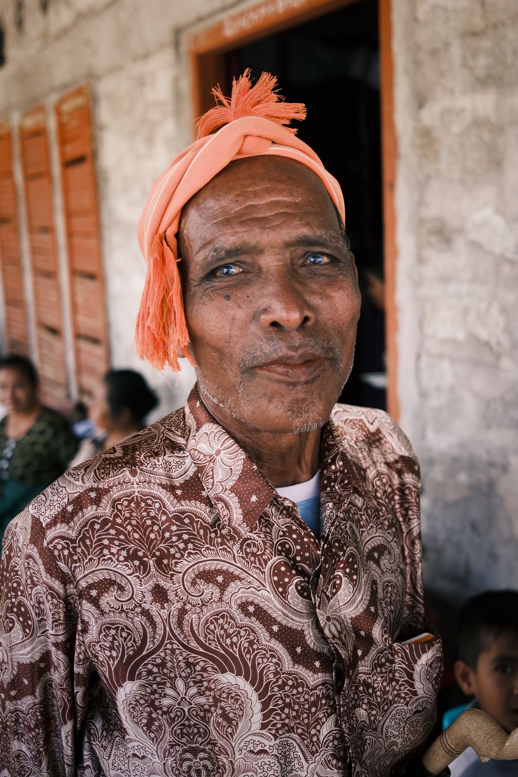 An elder in an orange headcloth and batik shirt