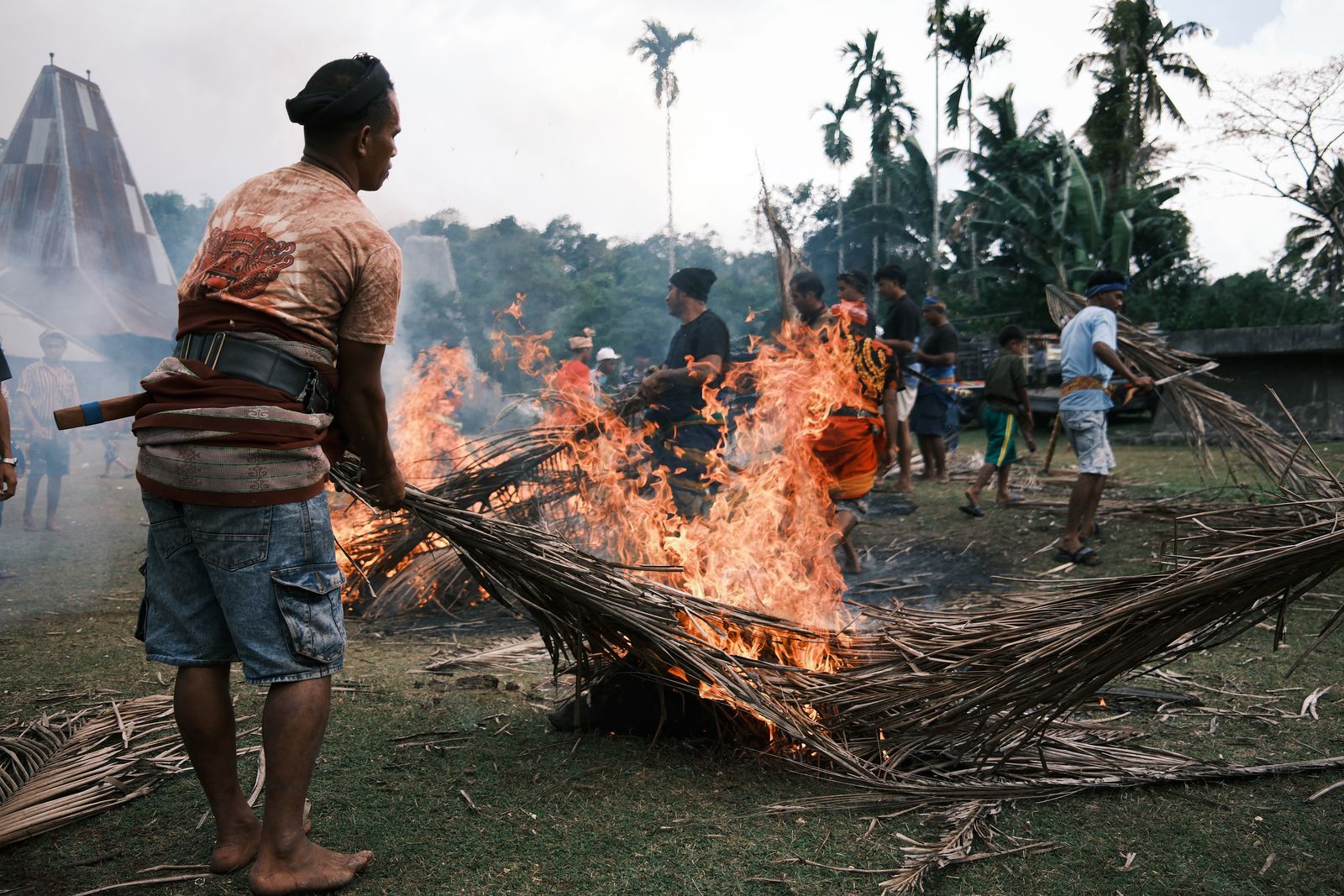 A man tending a fire of brush in a village clearing